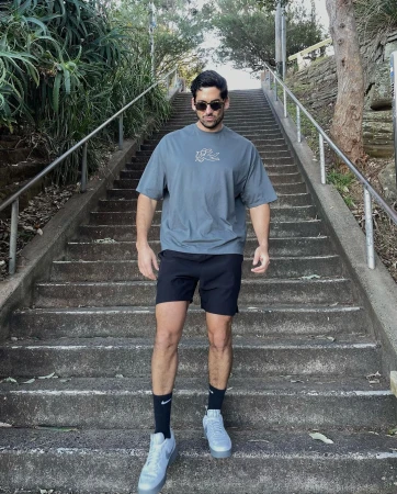 An adult male is walking down a long staircase in athletic wear, sunglasses, and sneakers, with greenery visible on the sides.