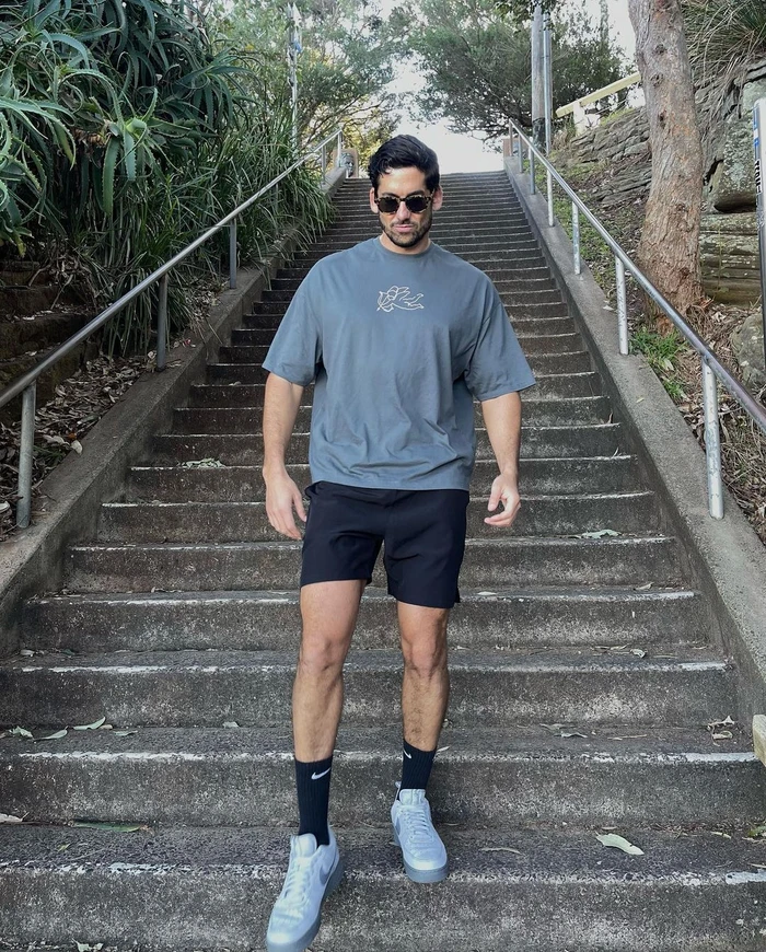 Man wearing sunglasses, grey t-shirt, black shorts, and sneakers descending outdoor concrete stairs in Sydney