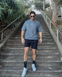 Man wearing sunglasses, grey t-shirt, black shorts, and sneakers descending outdoor concrete stairs in Sydney