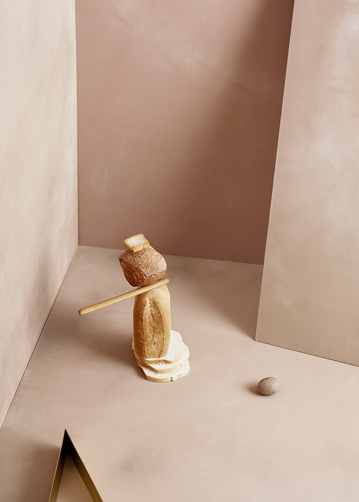 Creative still life of stacked sliced bread, baguette, and bread roll in an indoor studio setting with peach and tan color palette.