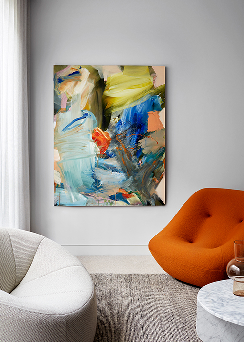 Abstract art painting hangs in a minimalist living room with a gray rug, a white chair, and an orange chair next to a marble table.