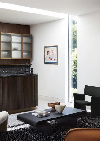 Modern interior living space featuring a dark coffee table, patterned rug, fluted wood bar, and artwork by Elisa Watson