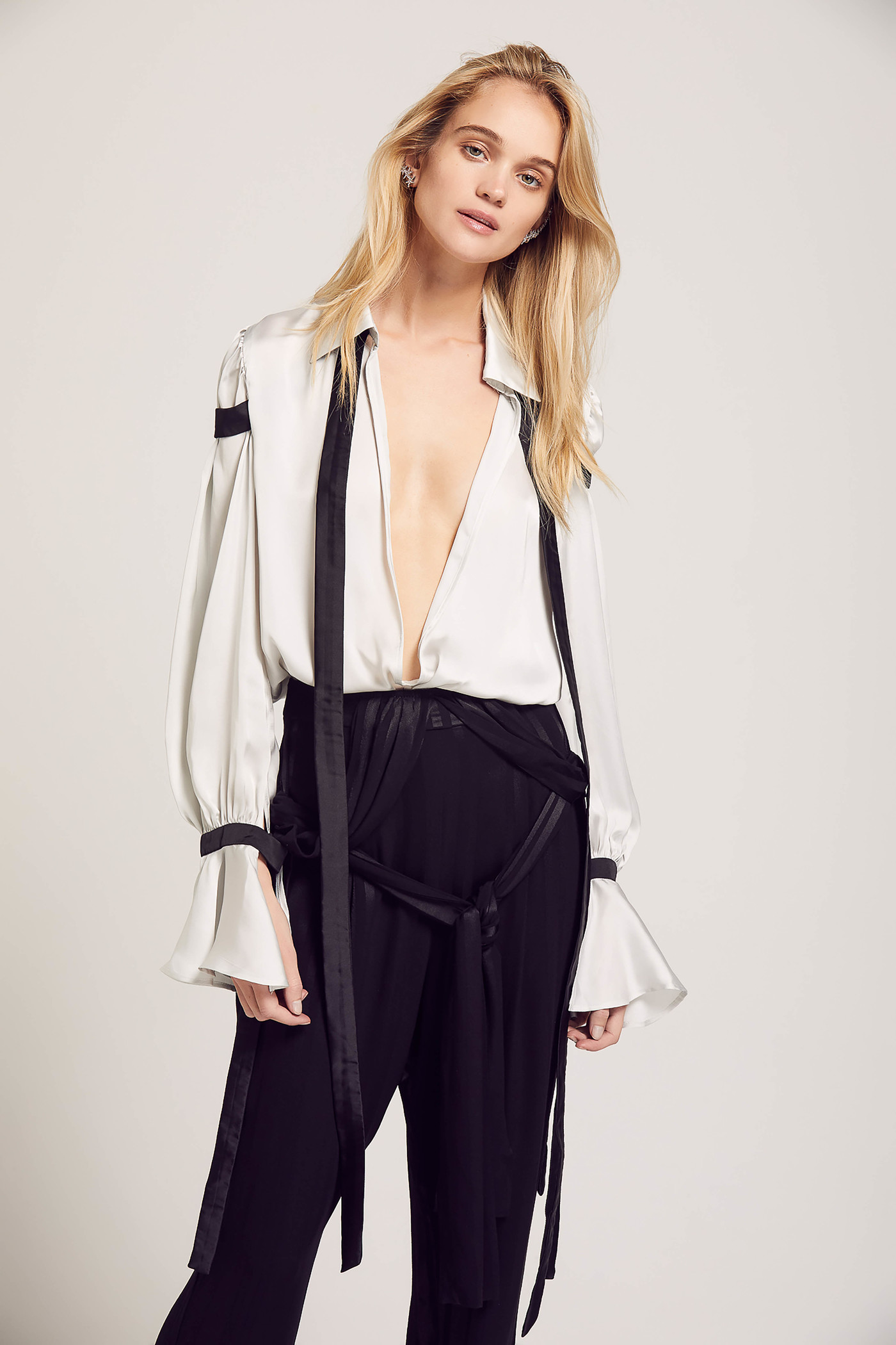 Elegant woman in a white blouse and black pants posing in front of a neutral background in a fashion photography studio setting.