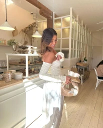 Smiling woman in an off-the-shoulder white top holding a coffee tray and handbag inside a cafe in Sydney