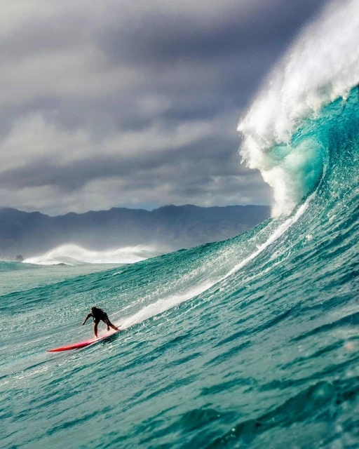 A surfer rides a large, turquoise ocean wave under a cloudy sky, showcasing the power of nature and a thrilling moment of athleticism.