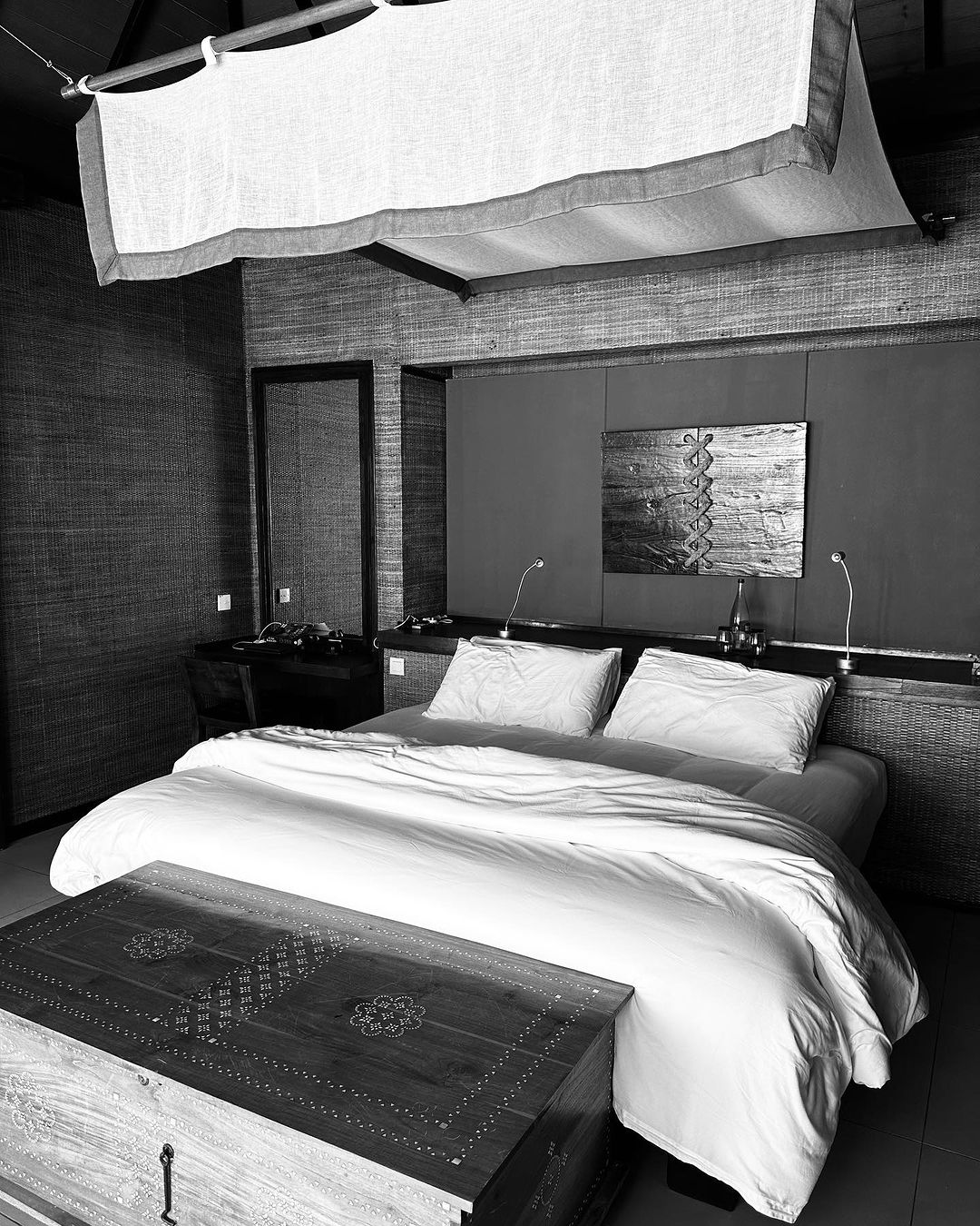 Monochrome hotel bedroom with a large bed featuring white linens and pillows, complemented by a wooden chest, creating a peaceful ambiance.