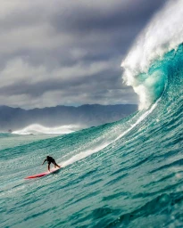 Surfer on a red surfboard riding a large turquoise wave under a dramatic overcast sky with distant mountains in the background