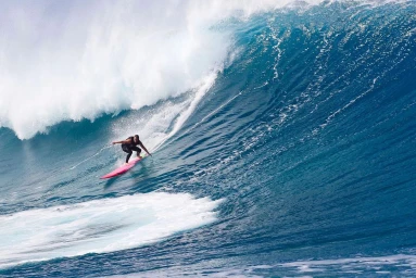 Surfer on a pink surfboard riding a large crashing ocean wave with white spray