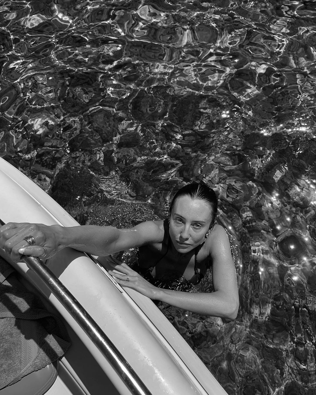 Black and white portrait of an adult female in water near a boat, featuring rippled water, monochrome tones, and natural sunlight.