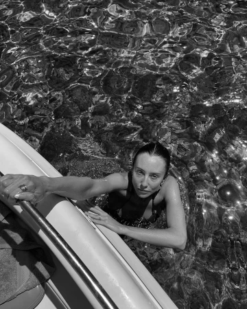 Monochrome overhead shot of a woman in the water holding onto the side of a boat