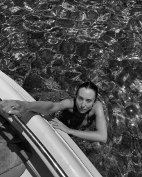 Monochrome overhead shot of a woman in the water holding onto the side of a boat