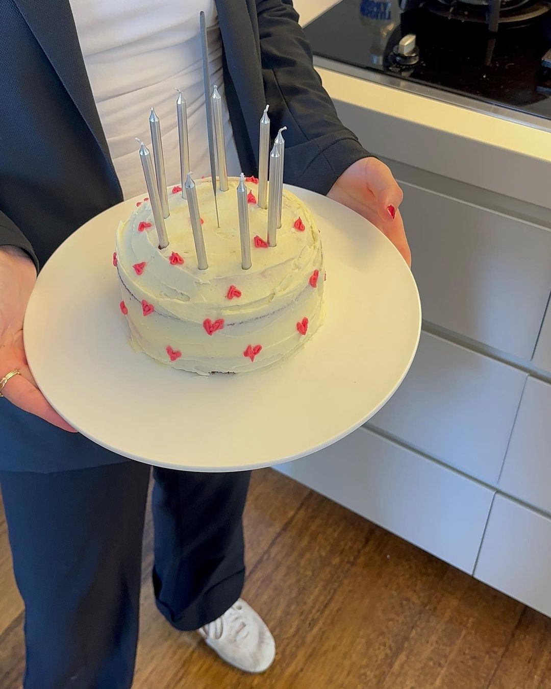 Celebratory moment with a two-tier cake adorned with lit candles, presented on a white plate in a bright indoor setting.