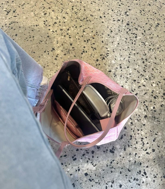 Overhead shot of a pink patterned tote bag on a speckled floor, containing a laptop, charger, and smaller cosmetic bag.