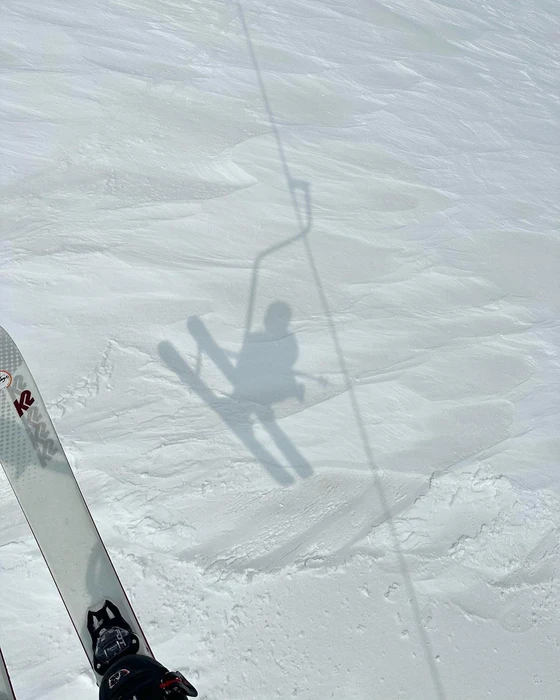 Overhead view of skis on a snowy slope casting a shadow of a skier on a chairlift