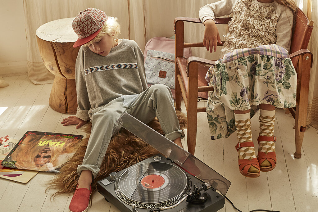 Two children, a boy and a girl, sit indoors with a record player and album covers creating a nostalgic and stylish scene.