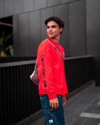 Young man wearing a bright red long-sleeve sweatshirt and blue jeans outdoors in Sydney, captured by Harvey Petito.