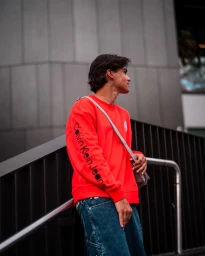 Young man in a vibrant red Calvin Klein sweatshirt and denim jeans standing outdoors near a railing in Sydney.