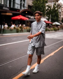 Young man walking on a city street wearing a patterned grey short-sleeve shirt and matching shorts with white sneakers