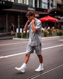 Young man walking on a city street wearing a matching patterned grey shirt and shorts with white high-top sneakers.