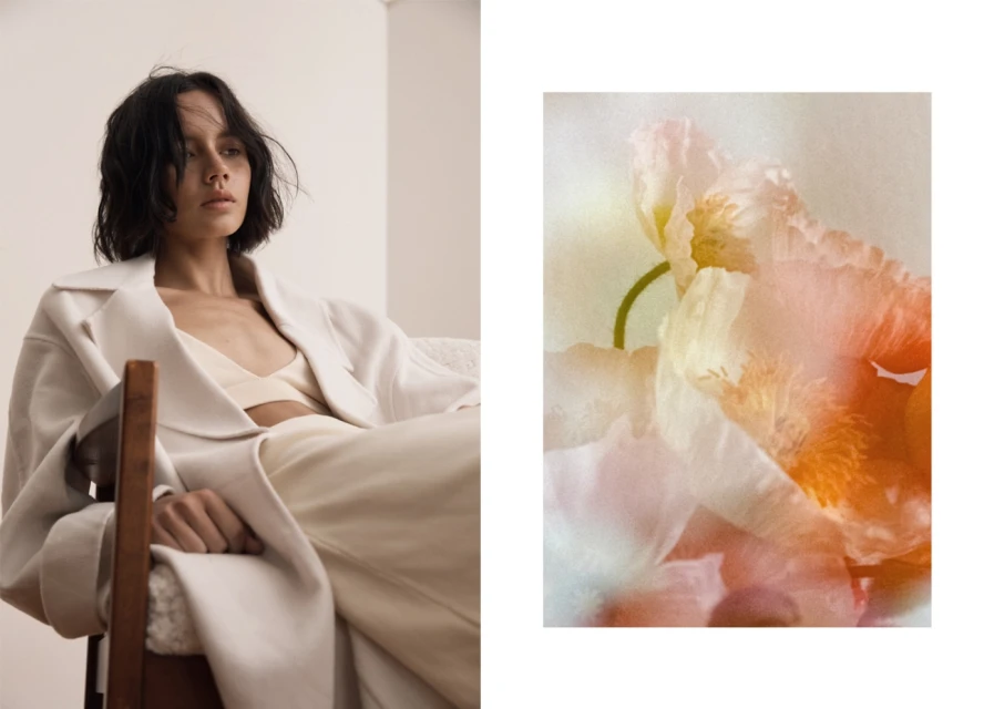 Woman in off-white attire sits in a wooden chair next to a floral image. Soft lighting and serene mood create a minimalist aesthetic.