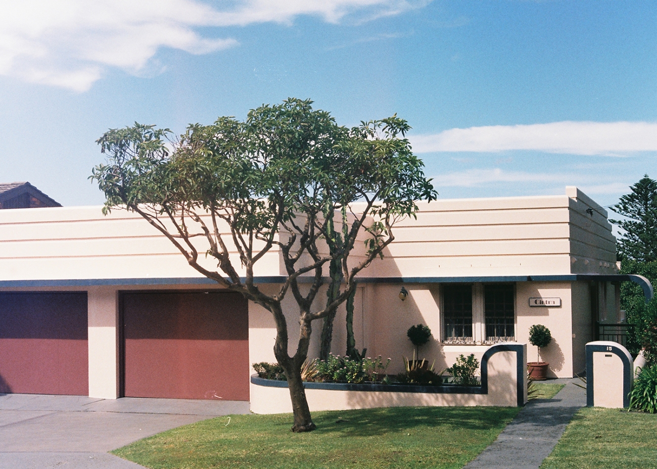 Exterior of a one-story home with a flat roof, light beige walls, and a neatly manicured lawn in front on a sunny day.