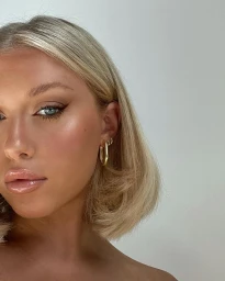 Close-up portrait of a woman with blonde bob hair wearing gold hoop earrings against a neutral background by Issy Quinn.