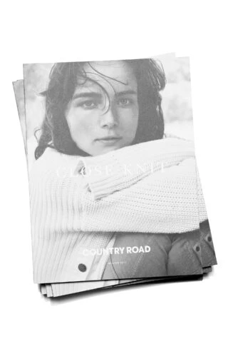 Monochrome magazine cover featuring a young woman with dark hair wearing a light-colored sweater, stacked with copies on a white surface.