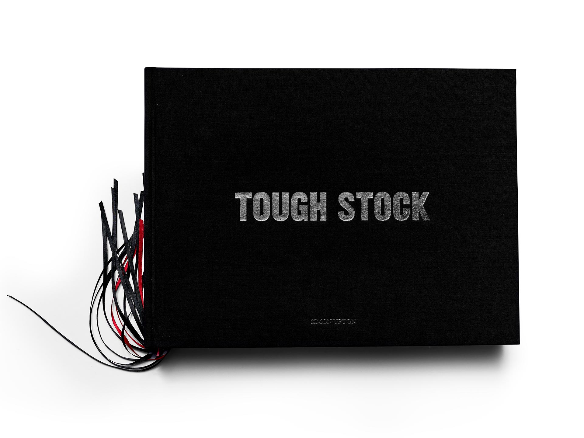 Close-up of a black hardcover book with silver lettering 'Tough Stock,' accented by black and red paper strips, against a white background.