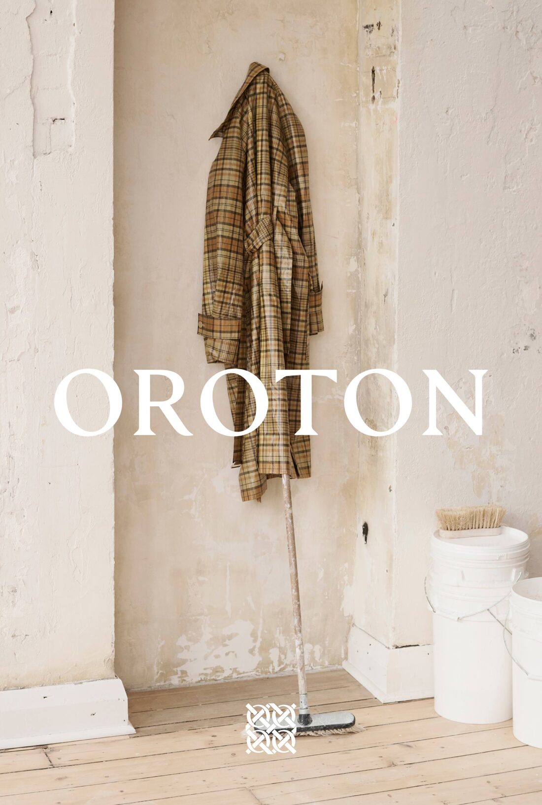 A plaid coat hangs in an alcove next to cleaning supplies and white paint cans, bathed in natural light with the brand name OROTON.