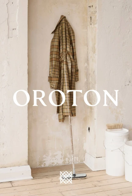 A plaid coat hangs in an alcove next to cleaning supplies and white paint cans, bathed in natural light with the brand name OROTON.