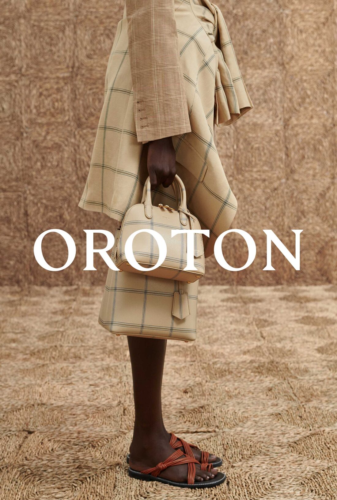 Fashion editorial shot showcasing a tan plaid skirt suit, small handbag, and leather sandals against a textured backdrop. 