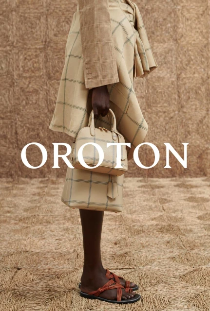 Fashion editorial shot showcasing a tan plaid skirt suit, small handbag, and leather sandals against a textured backdrop. 