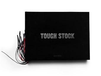 A closed black book featuring the title Tough Stock in silver lettering with dangling black and red ribbons.