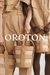 Two people wearing matching tan utility shirts and trousers, holding structured leather bucket bags against a neutral background.