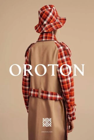 Model seen from behind wearing a plaid hat and a camel coat with plaid sleeves against a plain background