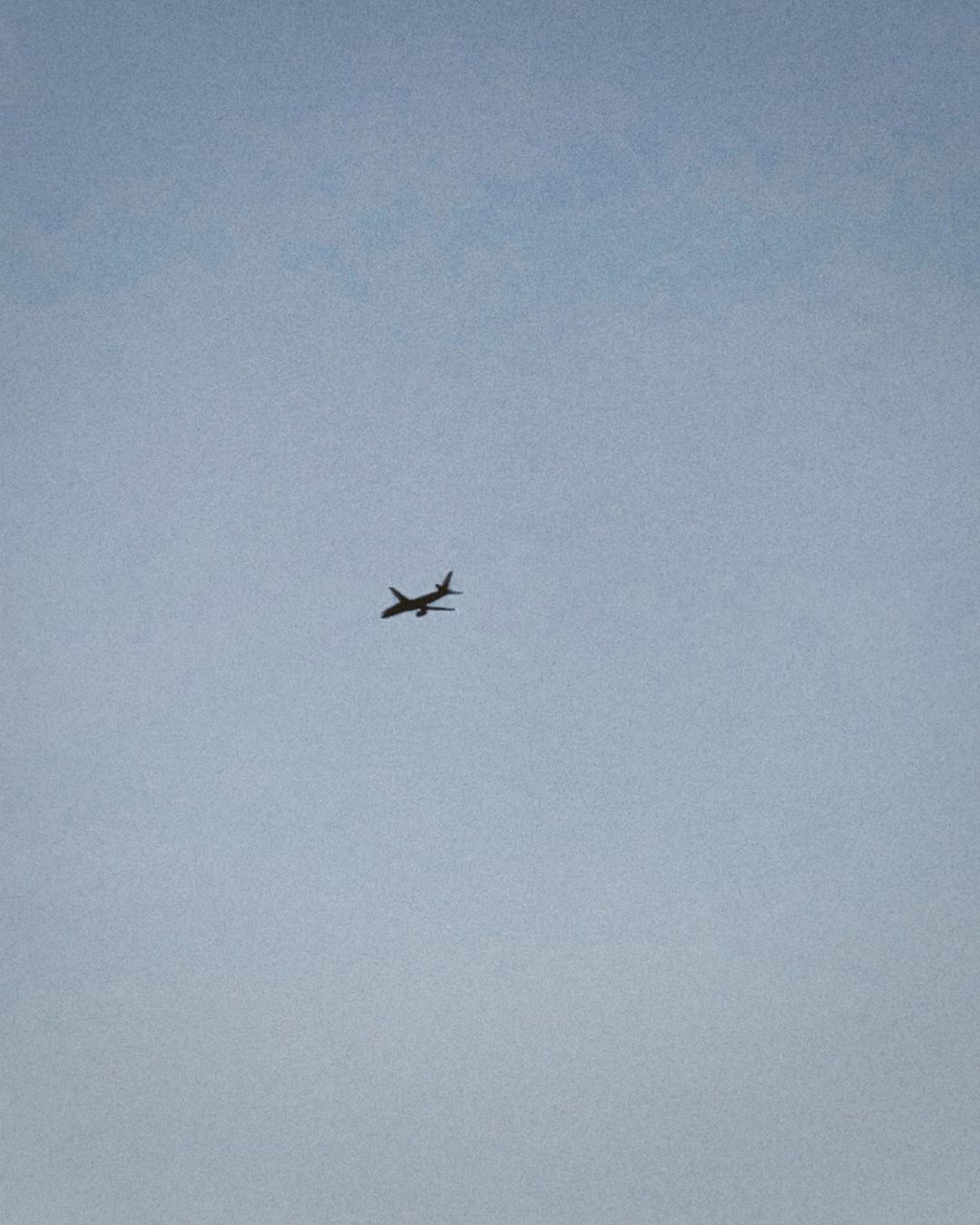 Airplane soars through a clear, pale blue sky. The plane, silhouetted, is the main focus of this simple, minimalist, aerial shot.