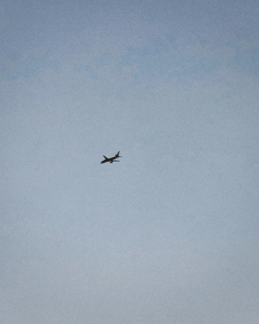 Airplane soars through a clear, pale blue sky. The plane, silhouetted, is the main focus of this simple, minimalist, aerial shot.