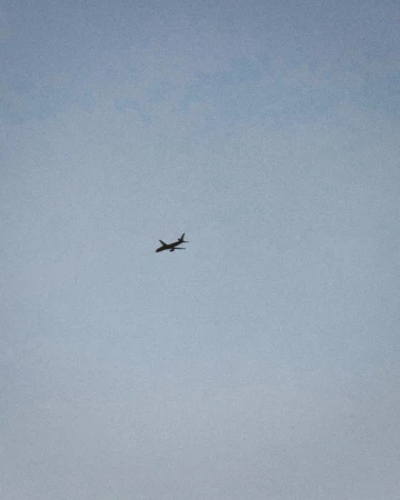 Airplane soars through a clear, pale blue sky. The plane, silhouetted, is the main focus of this simple, minimalist, aerial shot.