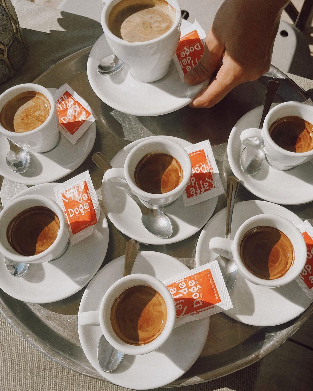 Overhead shot of a silver tray containing six white cups filled with coffee and sugar packets, creating a symmetrical and inviting layout.