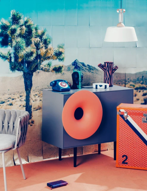 Interior setup with orange doughnut-shaped seat, gray cabinet holding home accessories, and a desert landscape background.