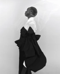 Black model wearing white collared shirt and black ruffled top with sheer veil in profile against white background