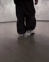 Low angle shot of a person wearing baggy dark trousers and light sneakers standing on a glossy concrete floor.