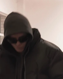Content creator Jai Waetford in dark sunglasses wearing a black puffer jacket with the hood up indoors.