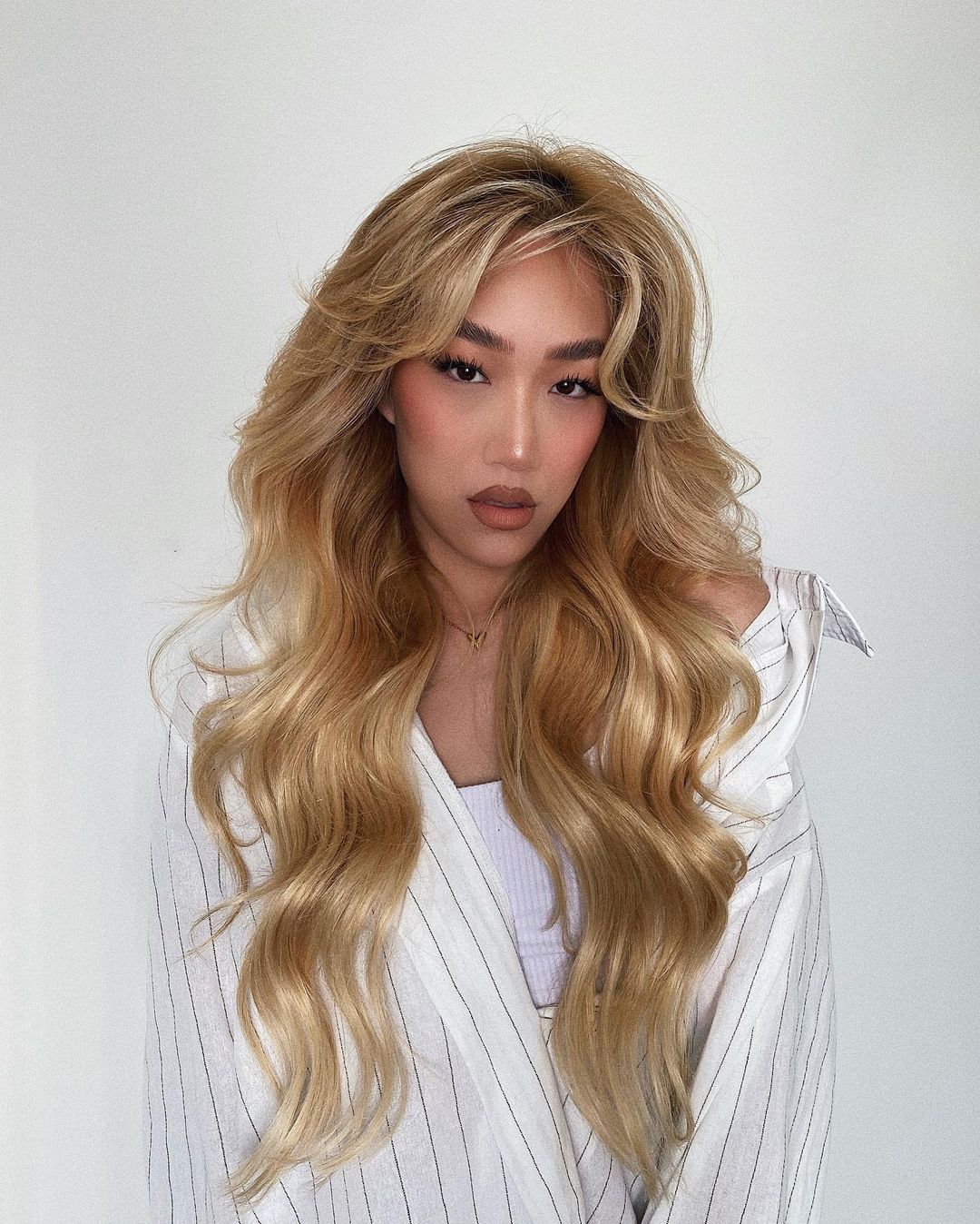 A woman with blond wavy hair poses wearing a striped shirt against a white background in a close-up portrait. Beauty shot.