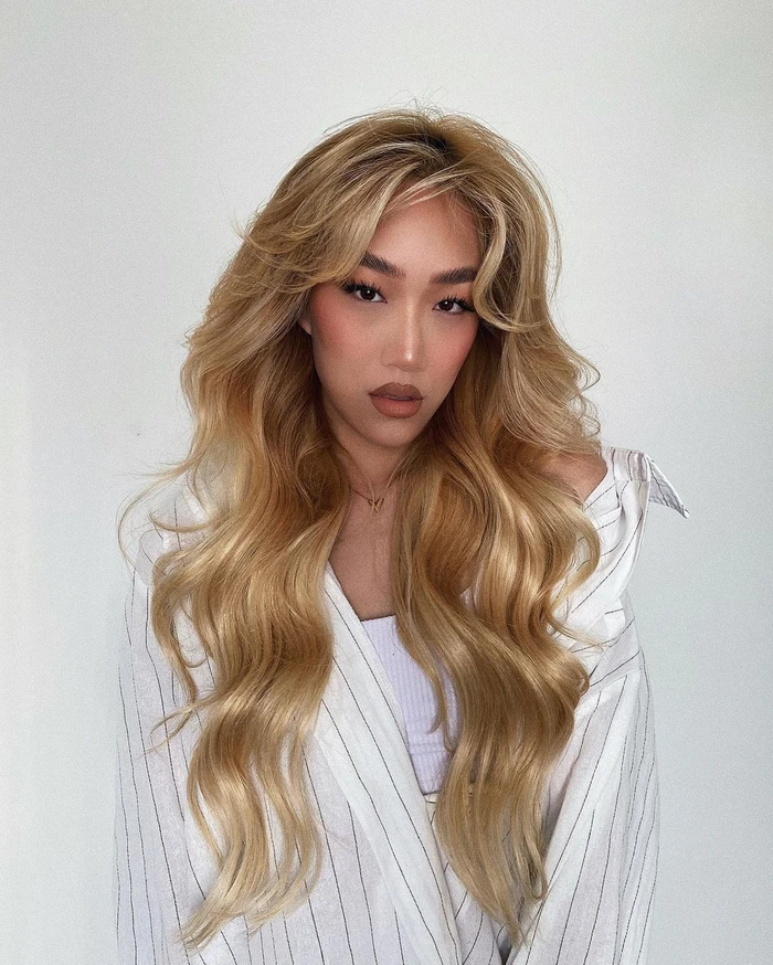 Portrait of a woman with long blonde wavy hair wearing a white pinstripe shirt against a plain white background