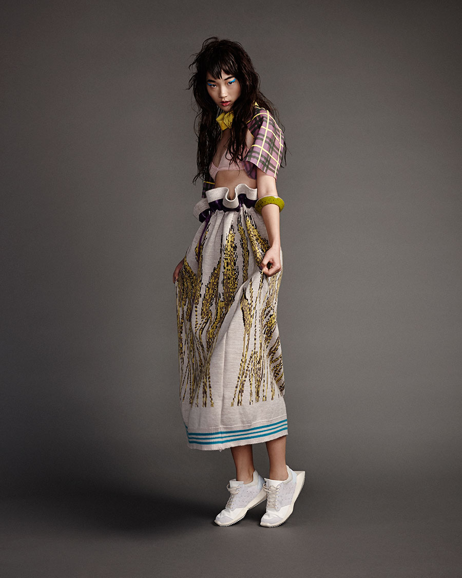 A young woman poses in a fashion shot wearing a bralette top and a long skirt with a giraffe print, complemented by white sneakers.
