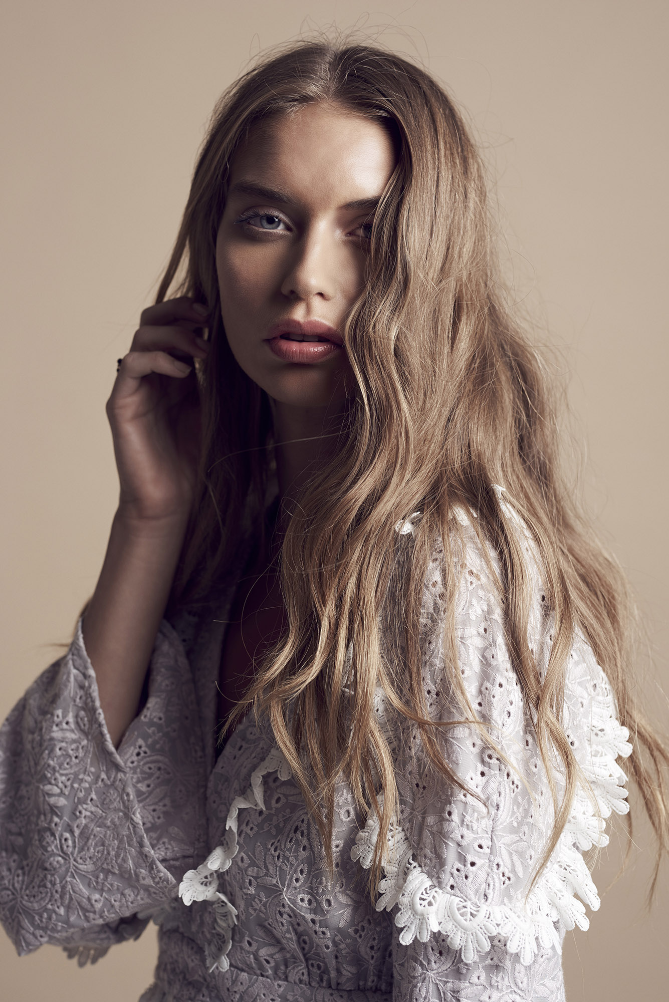 Portrait of a blonde female model wearing a white embroidered dress with make-up by Fern Madden against a neutral background