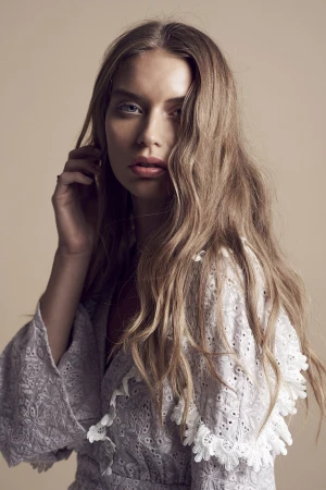 Portrait of a blonde female model wearing a white embroidered dress with make-up by Fern Madden against a neutral background