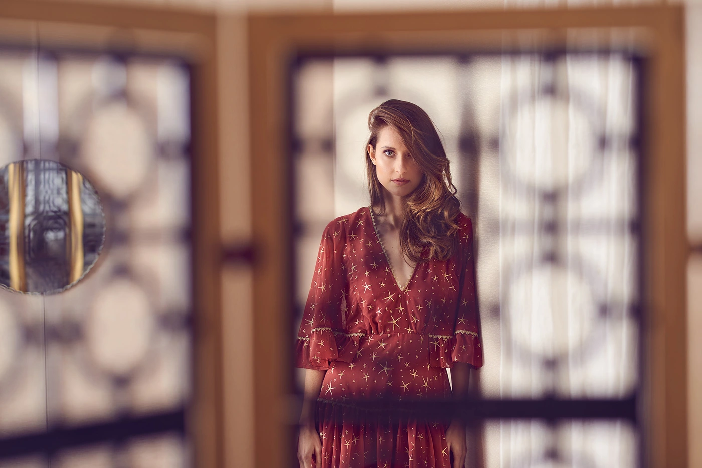 Woman with long brown hair wearing a red star-printed dress standing behind a patterned room divider.