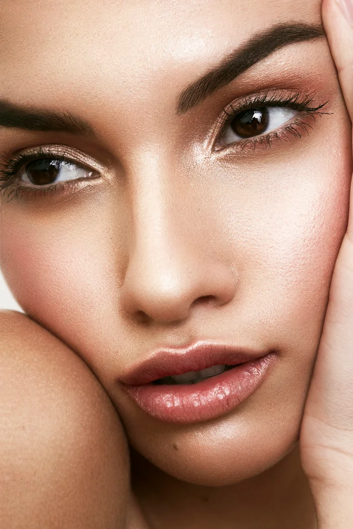 Close-up beauty portrait of a woman with dewy skin, glossy lips, and detailed eye makeup by Fern Madden.